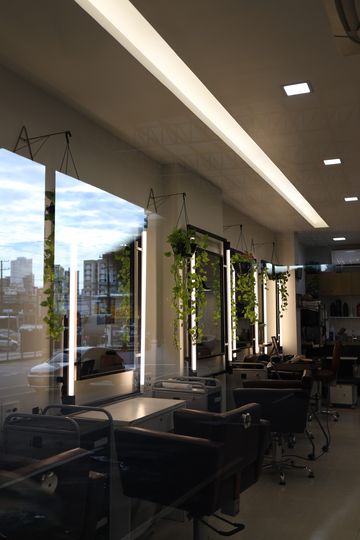 Salão do Constant Plaza visto da janela, com espelhos iluminados, plantas penduradas e as cadeiras ao fundo